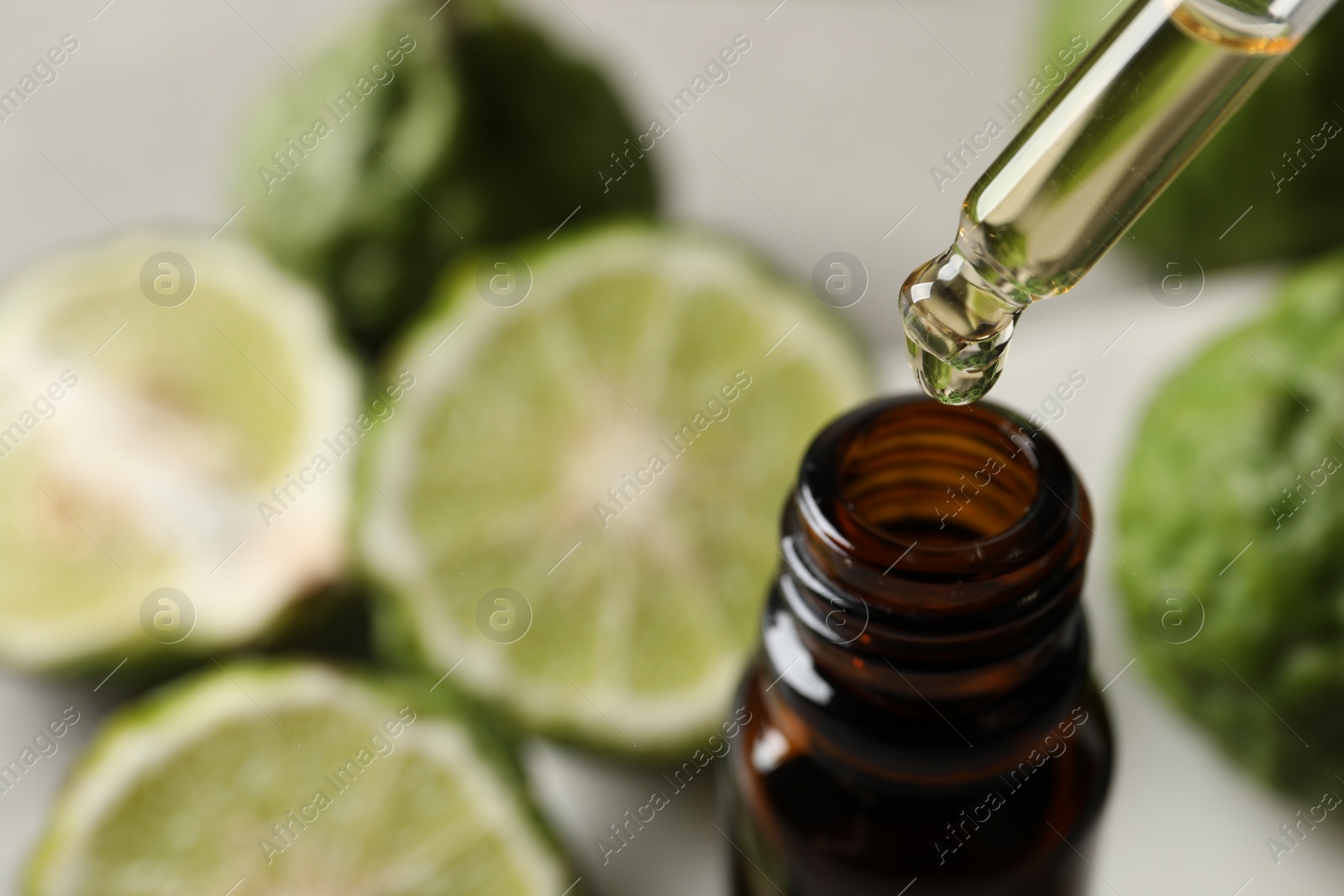 Photo of Dripping bergamot essential oil into glass bottle on table, closeup
