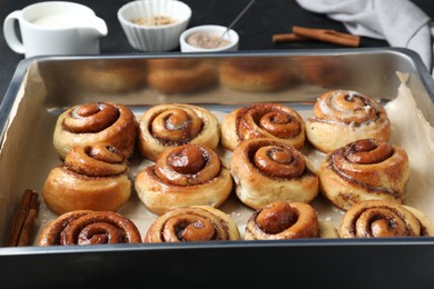 Photo of Baking dish with tasty cinnamon rolls on dark table
