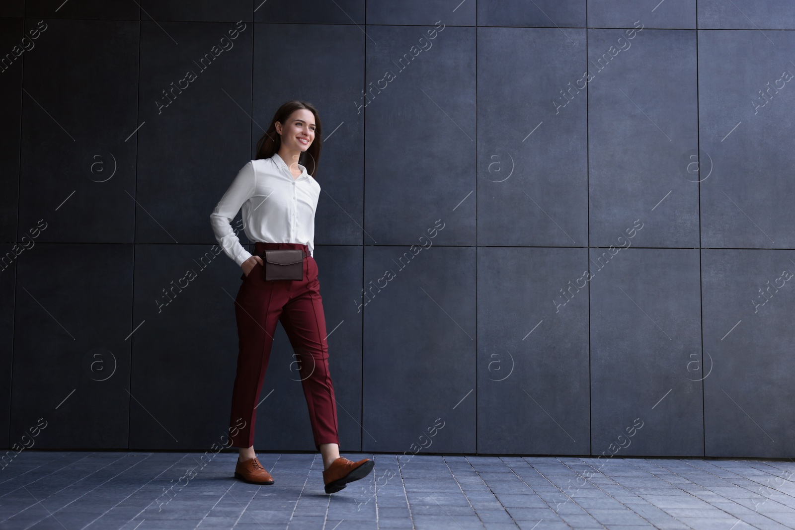 Photo of Young woman in formal clothes walking near grey wall outdoors, space for text