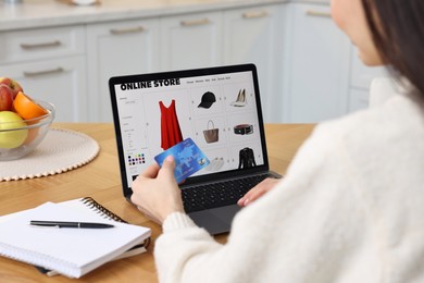 Photo of Woman with laptop and credit card shopping online at wooden table in kitchen, closeup