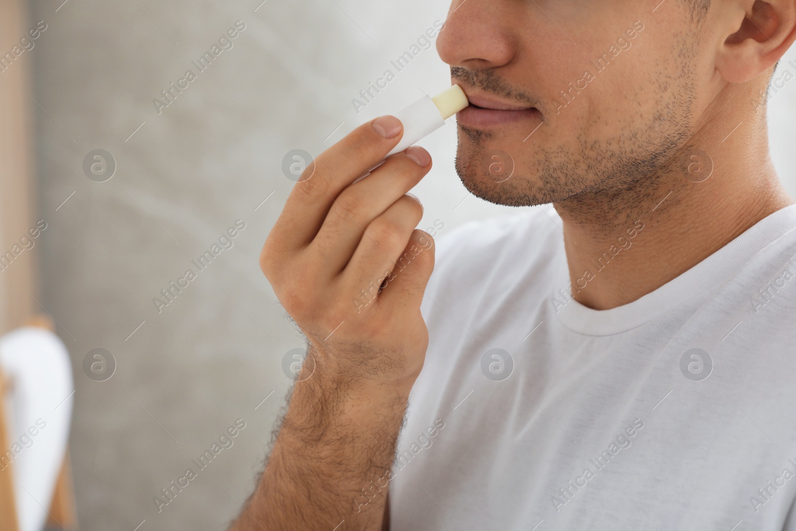 Photo of Man applying hygienic lip balm indoors, closeup