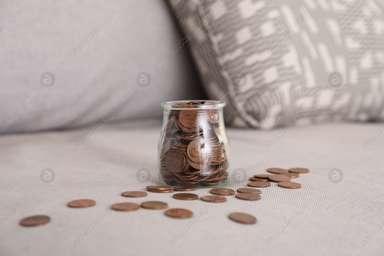 Photo of Glass jar with coins on grey sofa