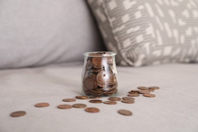 Photo of Glass jar with coins on grey sofa