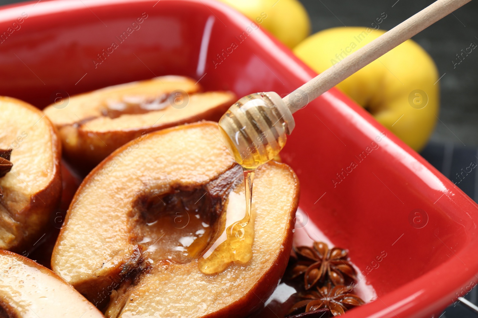 Photo of Pouring tasty honey onto baked quinces in dish on table, closeup