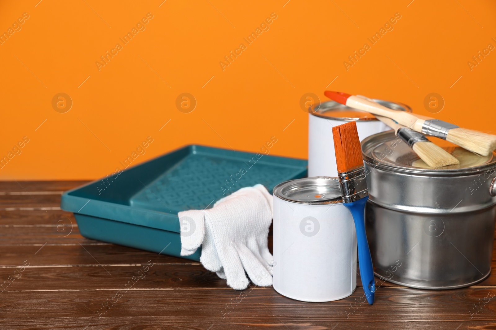 Photo of Can with paint, brush and renovation equipment on wooden table against orange background