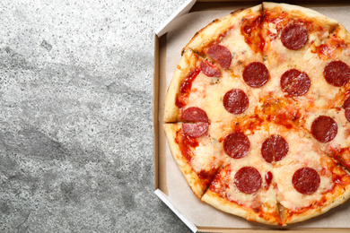 Photo of Hot delicious pepperoni pizza in cardboard box on grey table, top view. Space for text