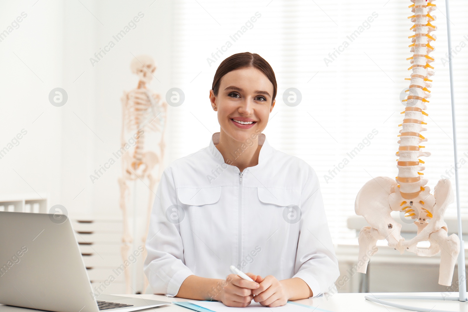 Photo of Female orthopedist with laptop near human spine model in office