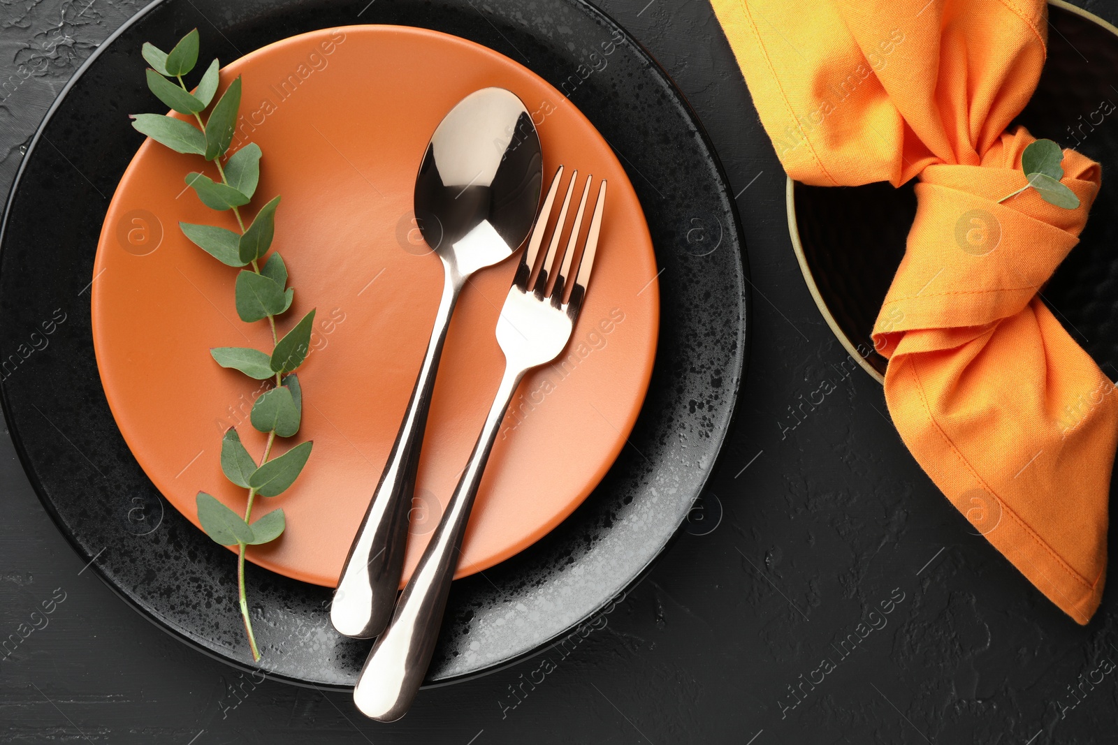 Photo of Stylish setting with cutlery, eucalyptus branch, napkin and plates on dark textured table, flat lay