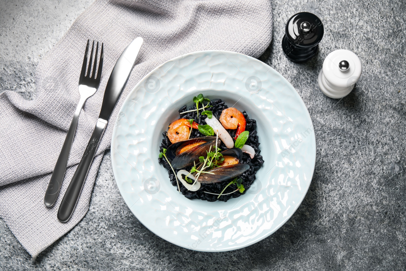 Photo of Delicious black risotto with seafood served on grey table, flat lay