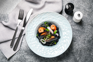 Photo of Delicious black risotto with seafood served on grey table, flat lay