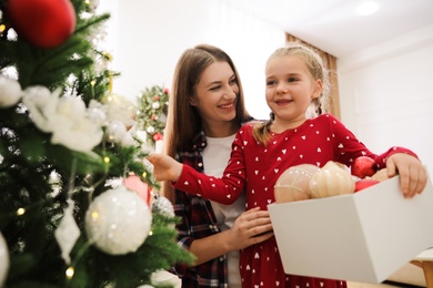 Photo of Happy mother with her cute daughter decorating Christmas tree together at home