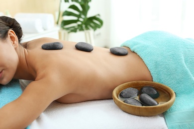 Beautiful young woman getting hot stone massage in spa salon