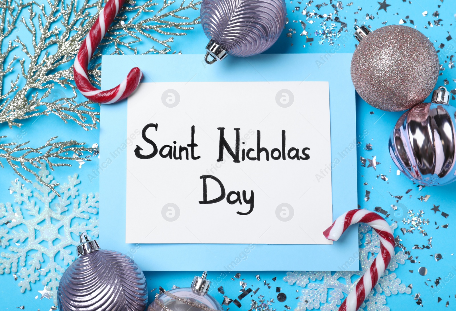 Photo of Card with text Saint Nicholas Day and festive decor on light blue background, flat lay