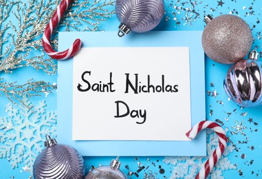 Photo of Card with text Saint Nicholas Day and festive decor on light blue background, flat lay