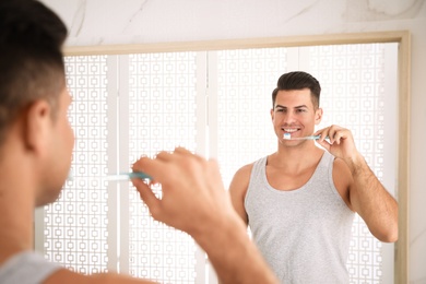 Photo of Man brushing teeth in front of mirror at home