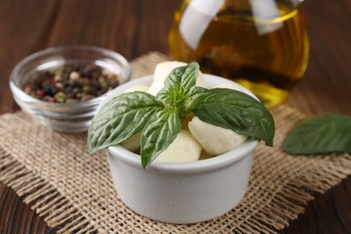 Photo of Tasty mozarella balls and basil leaves in bowl on table, closeup