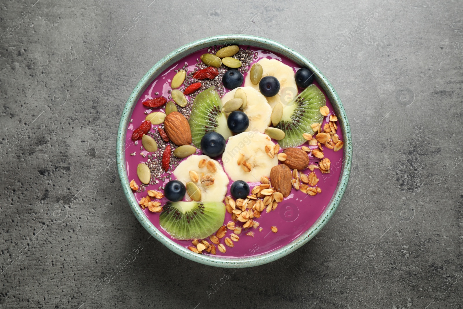 Photo of Delicious acai smoothie with granola and fruits on grey table, top view