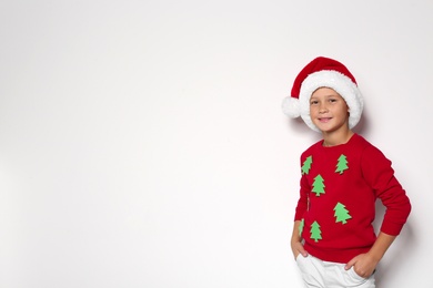 Photo of Cute little boy in handmade Christmas sweater and hat on white background. Space for text