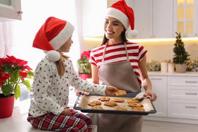 Photo of Mother giving her cute little daughter freshly baked Christmas cookies in kitchen