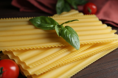 Photo of Uncooked lasagna sheets with basil on wooden table, closeup