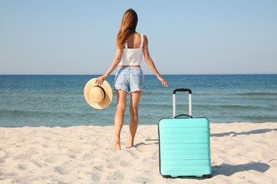Photo of Woman walking to sea and suitcase on beach, back view