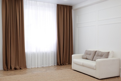 Photo of Sofa and window with brown curtains in simple room interior