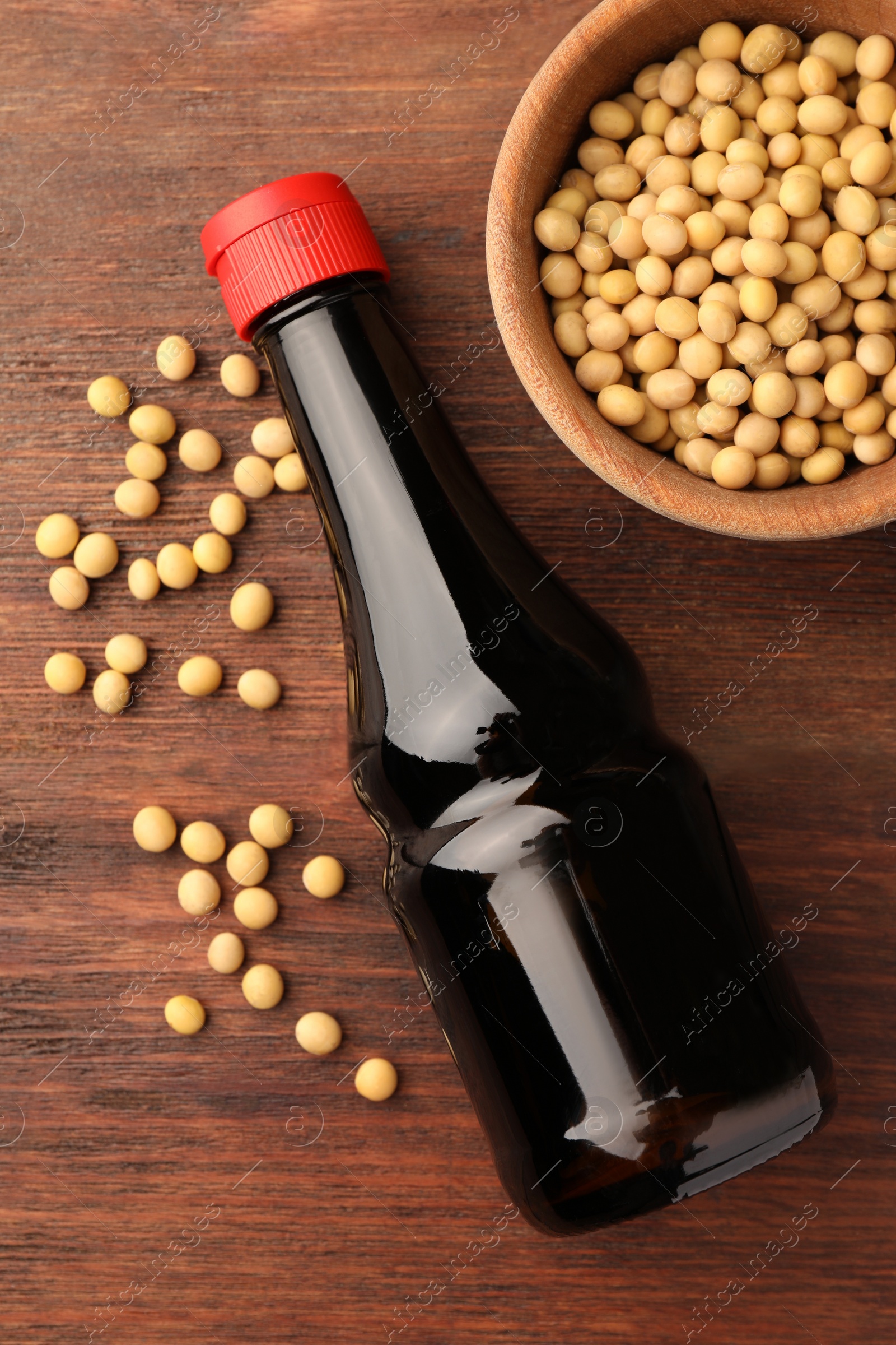 Photo of Bottle of soy sauce and soybeans on wooden table, flat lay