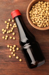 Photo of Bottle of soy sauce and soybeans on wooden table, flat lay