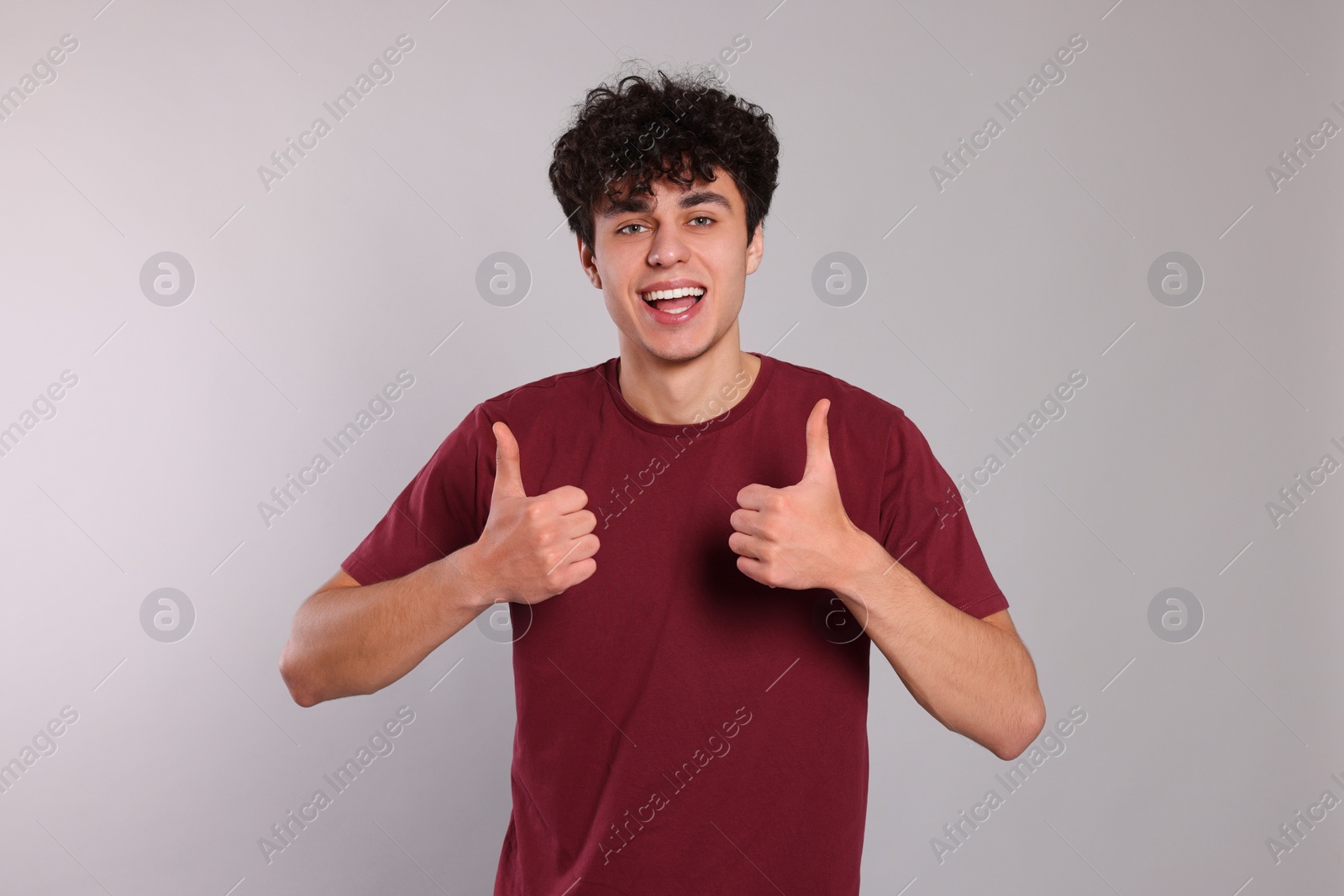 Photo of Handsome young man showing thumbs up on light grey background