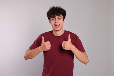 Handsome young man showing thumbs up on light grey background