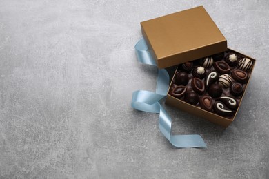 Open box of delicious chocolate candies and color ribbon on light grey table, flat lay. Space for text