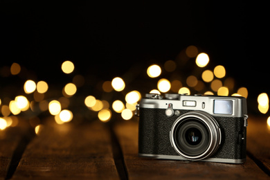 Photo of Vintage camera on wooden table against festive lights, space for text. Bokeh effect