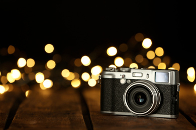 Vintage camera on wooden table against festive lights, space for text. Bokeh effect