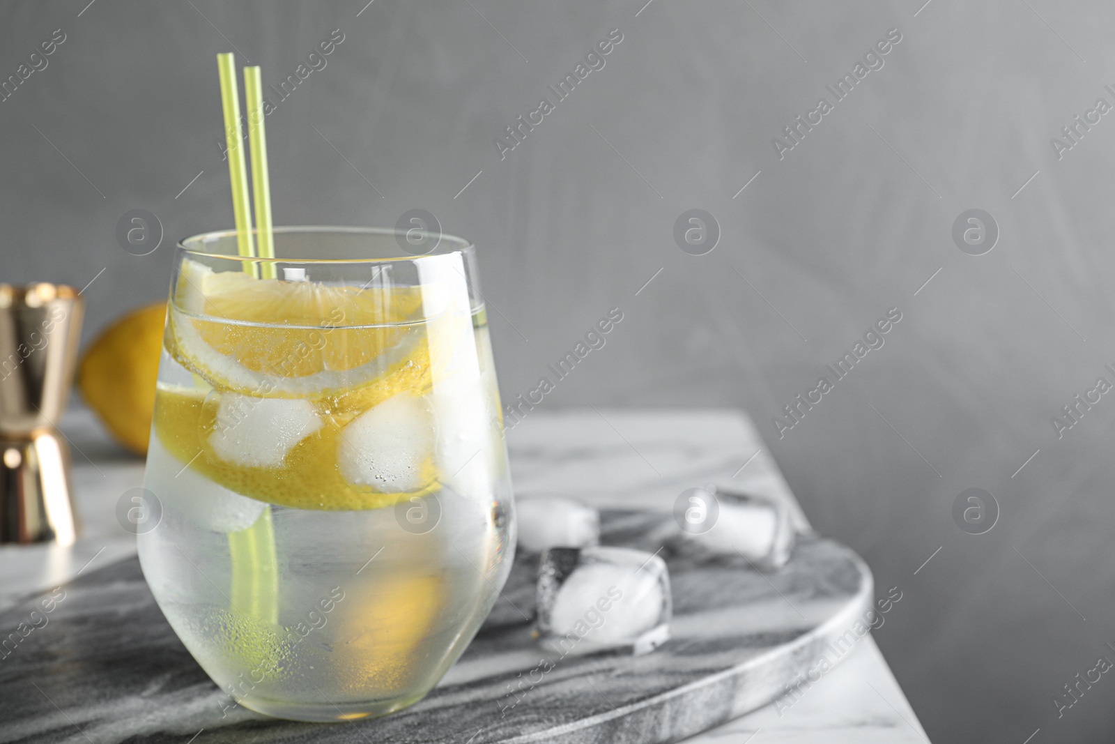 Photo of Glass of cocktail with vodka, ice and lemon on grey table. Space for text