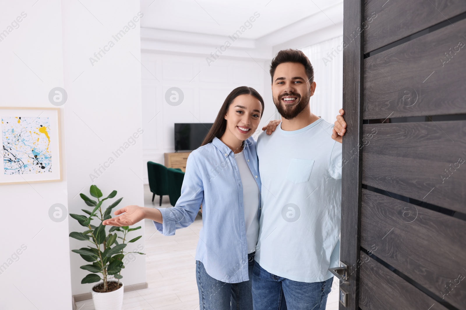 Photo of Happy couple welcoming near door. Invitation to come indoors