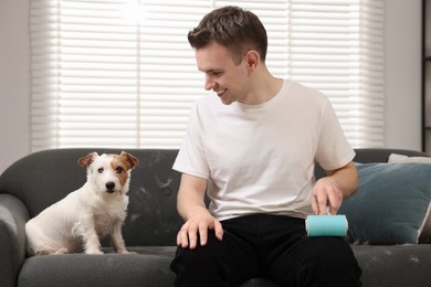 Photo of Pet shedding. Smiling man with lint roller removing dog's hair from pants at home