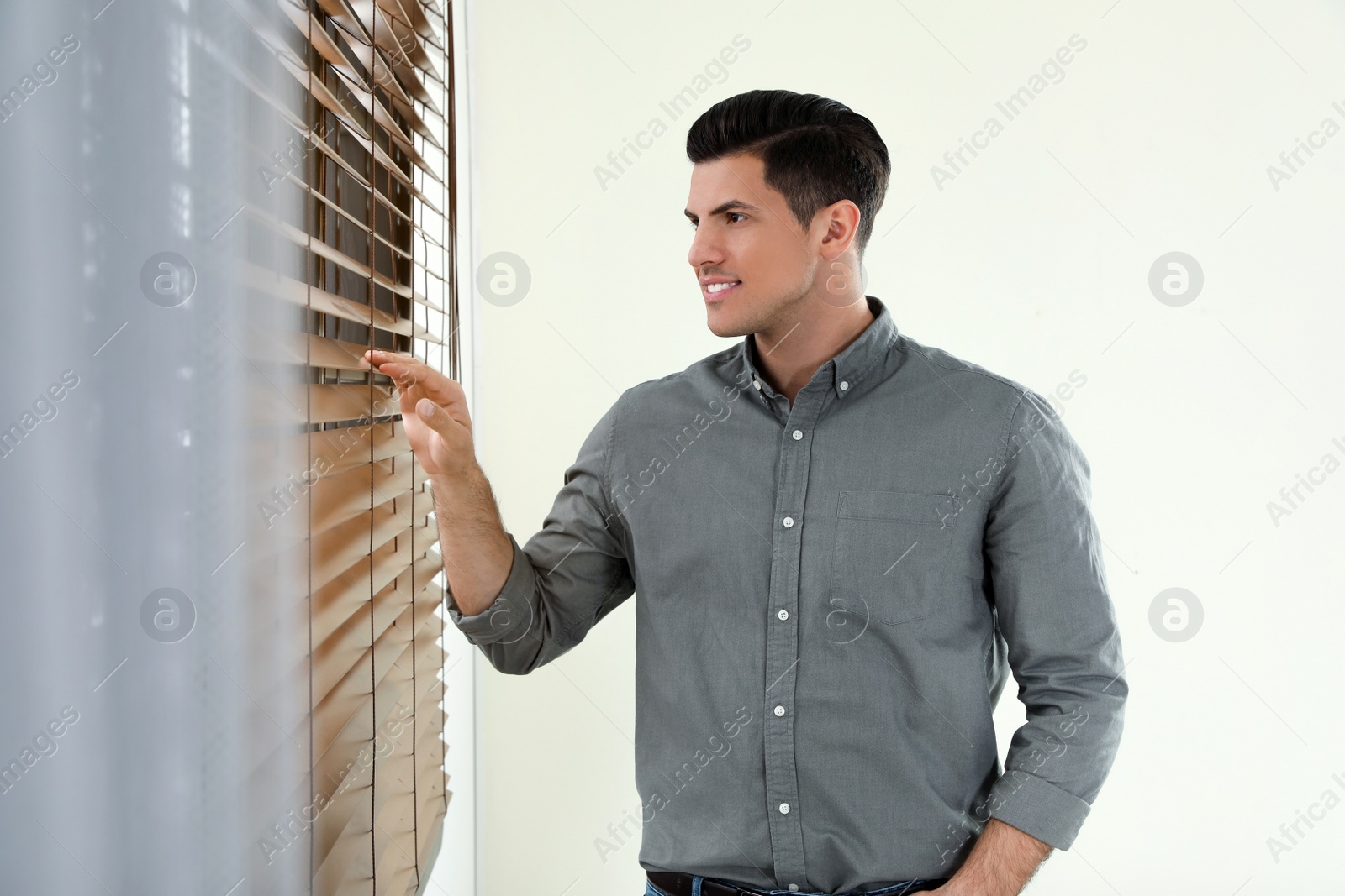 Photo of Handsome man looking through window blinds indoors