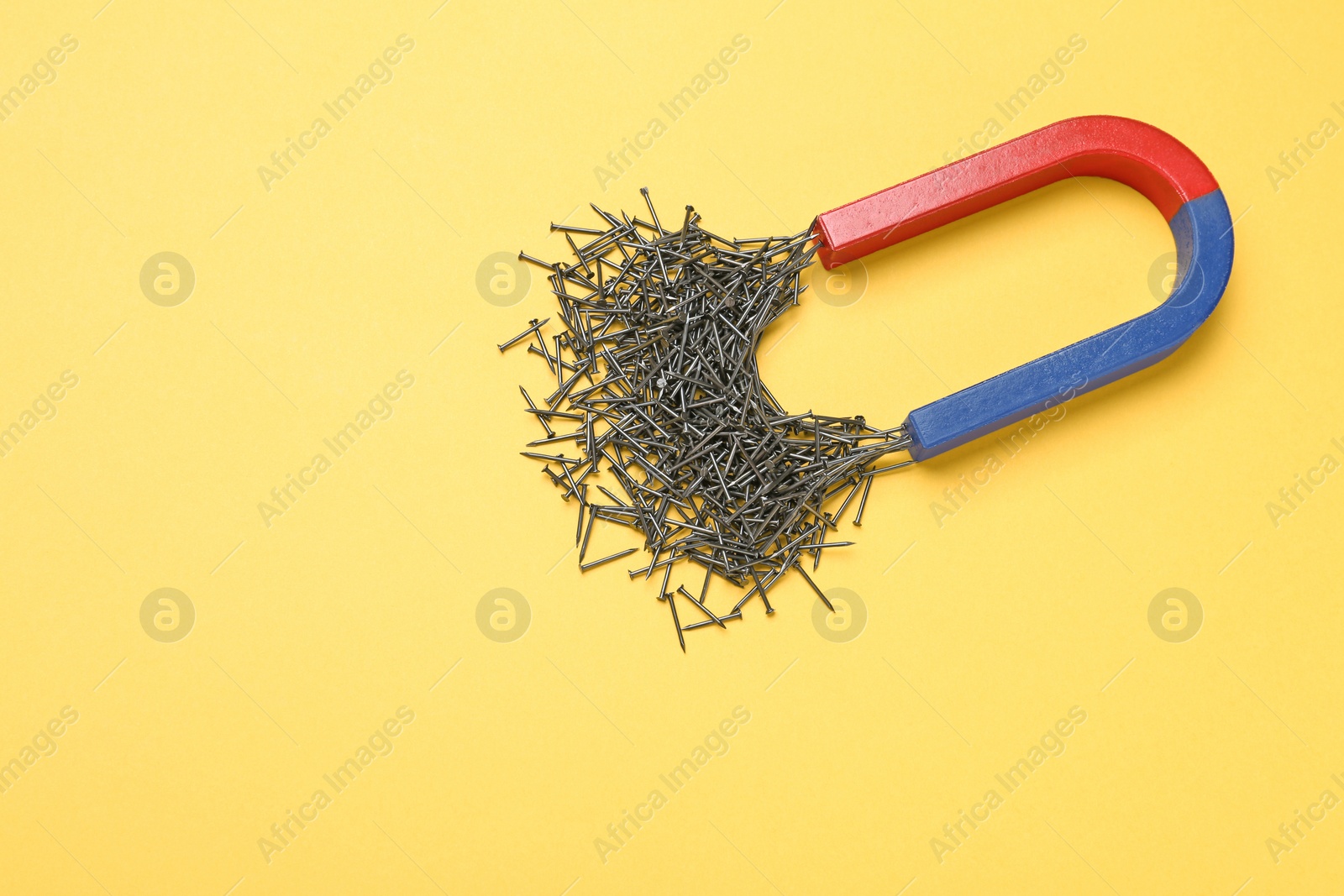 Photo of Magnet attracting nails on color background, top view with space for text