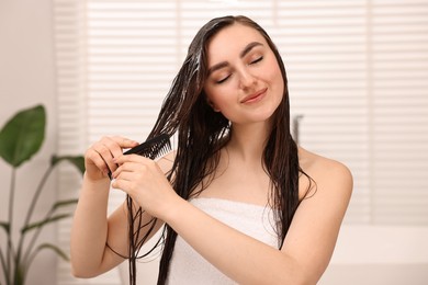 Photo of Young woman brushing hair after applying mask in bathroom