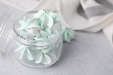 Photo of Tasty meringue cookies in glass jar on light grey table