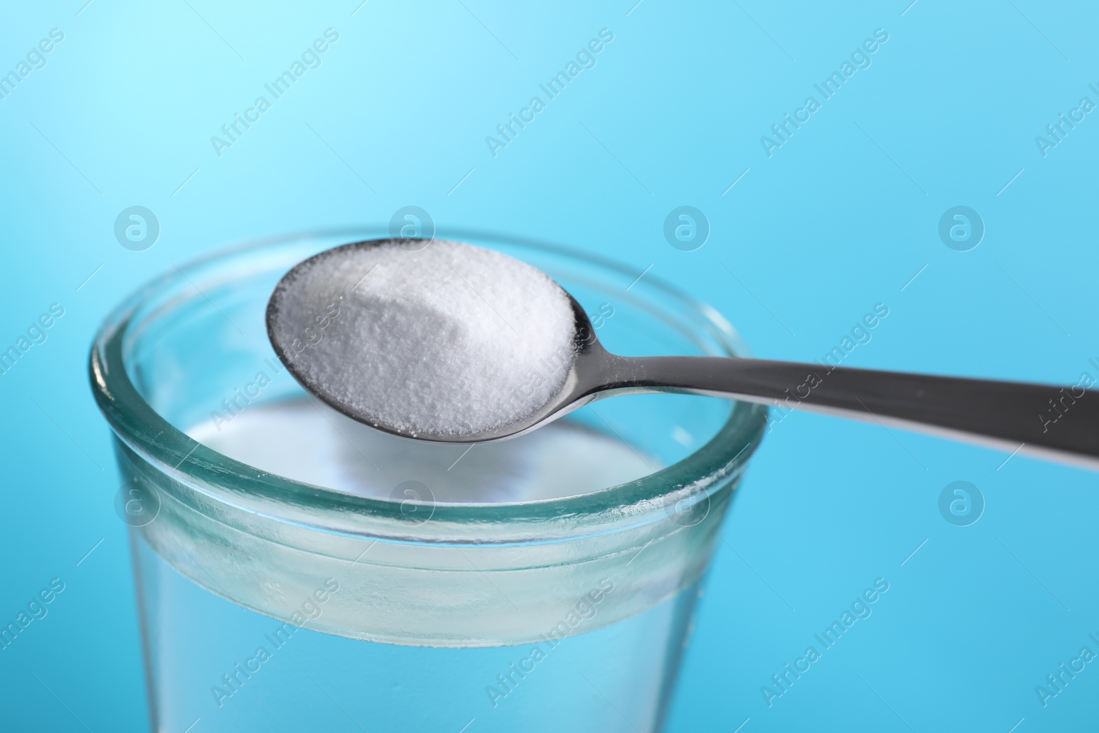 Photo of Adding baking soda into glass of water on light blue background, closeup