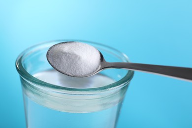 Photo of Adding baking soda into glass of water on light blue background, closeup