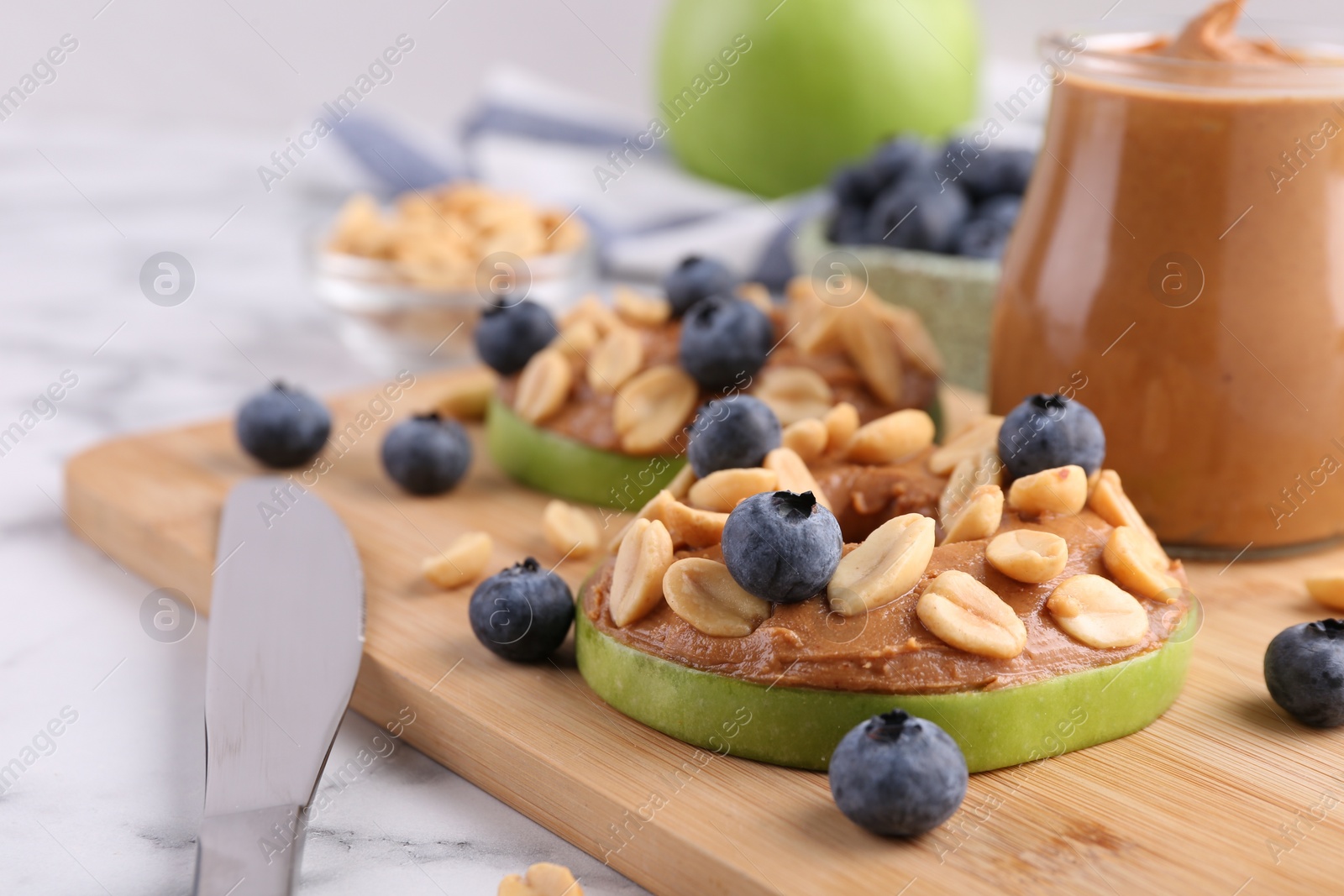 Photo of Slices of fresh apple with peanut butter, blueberries and nuts on white marble table, closeup