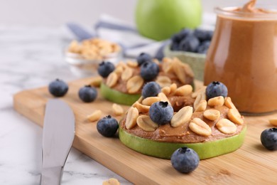 Slices of fresh apple with peanut butter, blueberries and nuts on white marble table, closeup