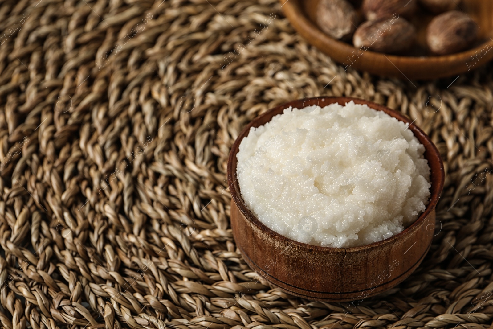 Photo of Shea butter in bowl and nuts on wicker mat, closeup. Space for text