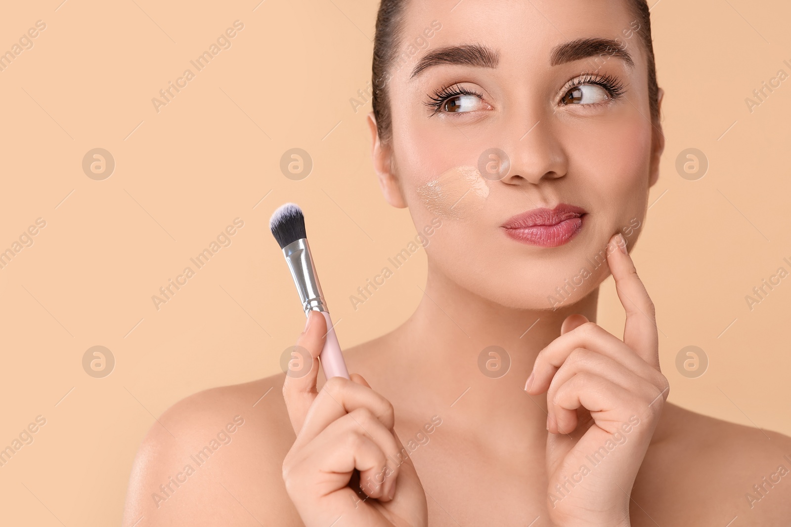 Photo of Woman with swatch of foundation holding makeup brush on beige background. Space for text