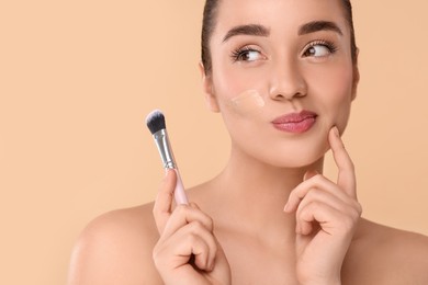 Photo of Woman with swatch of foundation holding makeup brush on beige background. Space for text