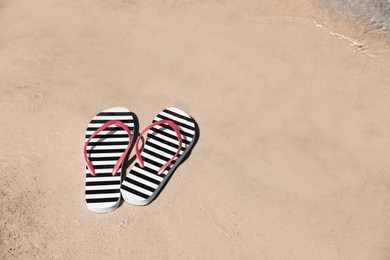 Stylish flip flops on sandy beach near sea, space for text