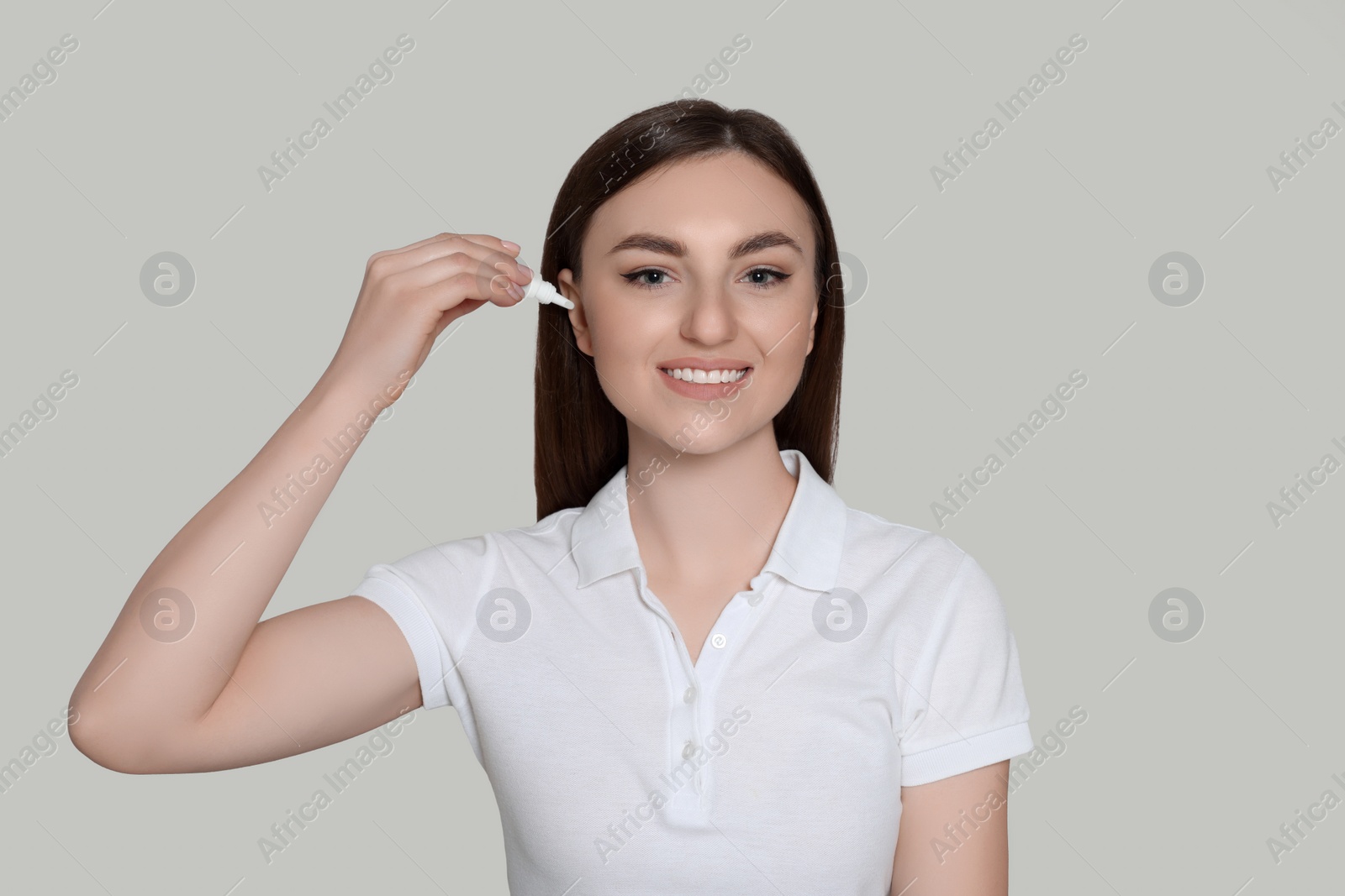 Photo of Young woman using ear drops on light grey background