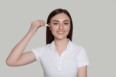 Young woman using ear drops on light grey background